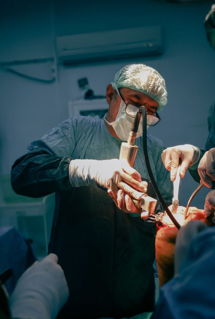 A surgeon operates in an operating room wearing surgical attire.