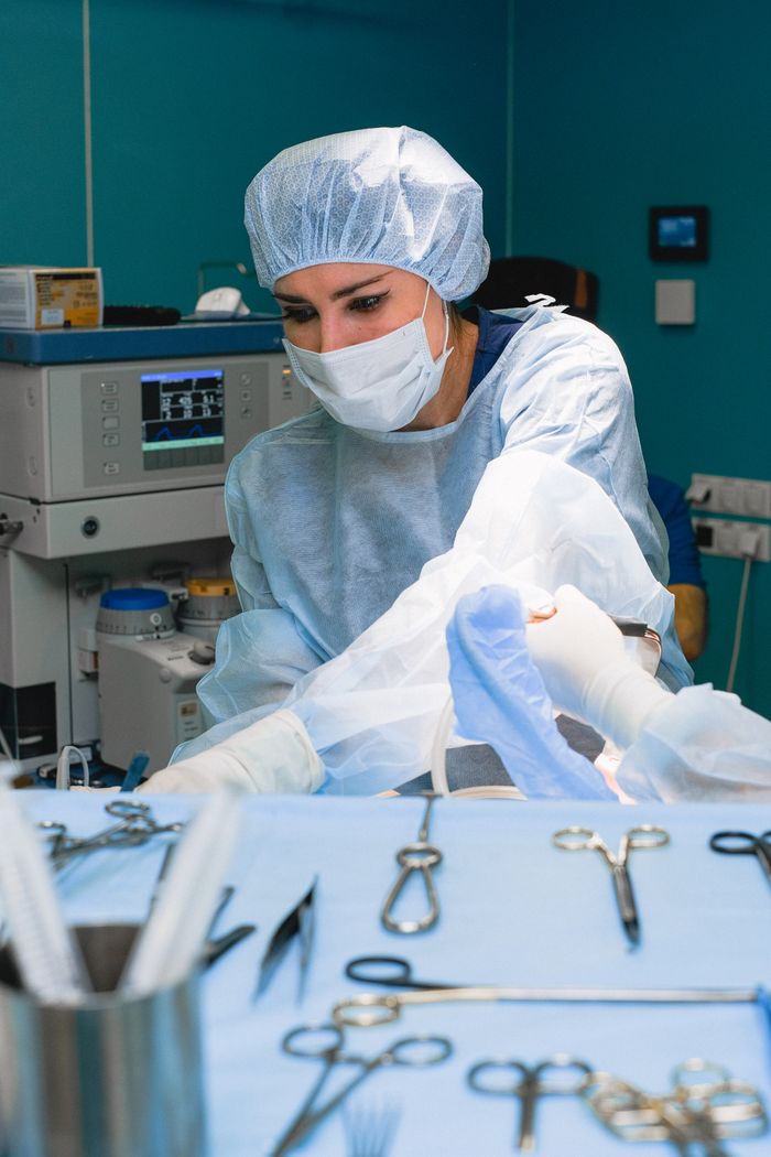 A female surgeon focuses on a procedure, surrounded by surgical tools in a hospital operating room.